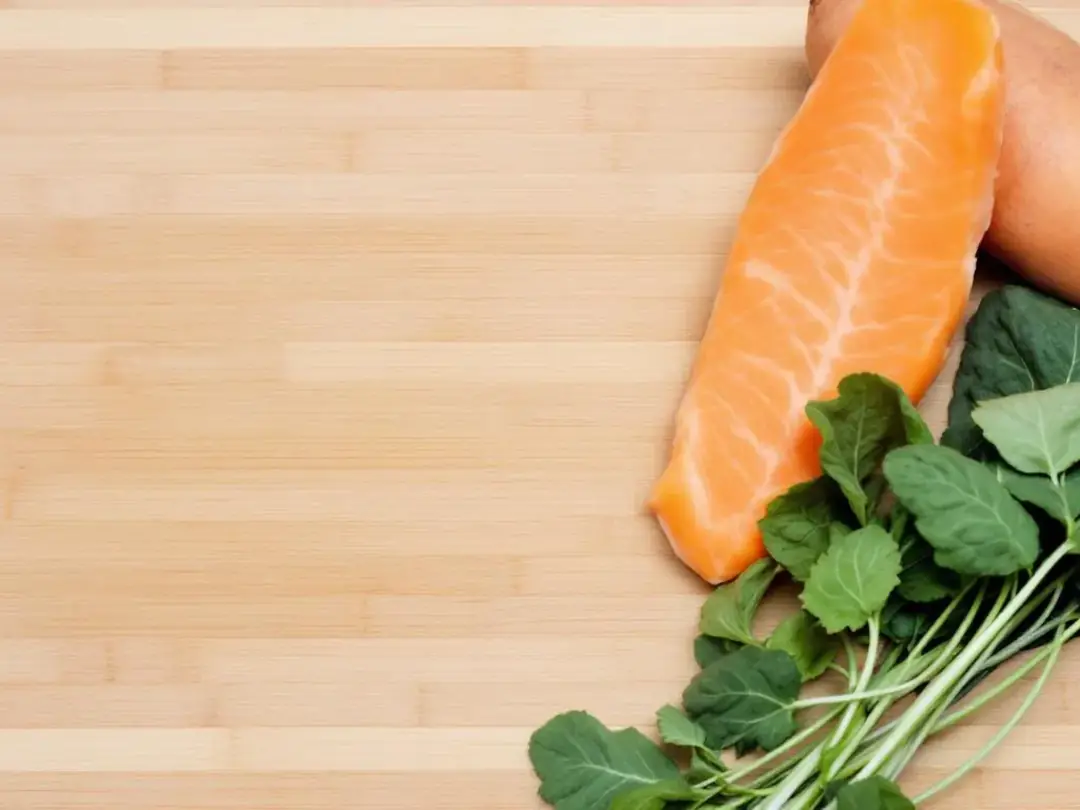 The image features a cutting board topped with fresh ingredients, including vibrant salmon fillets, orange sweet...