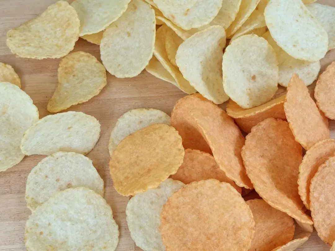 The image shows a variety of chips spread out on a table, including potato chips, tortilla chips, and sweet potato...